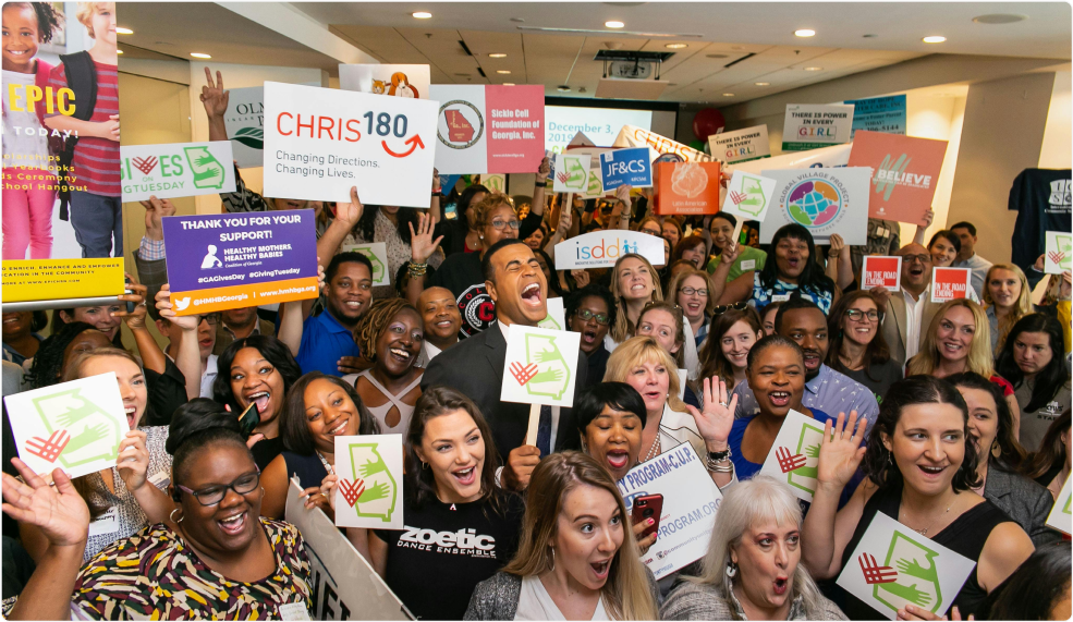 Large group of diverse people cheering and holding signs at an indoor charity auction fundraiser.