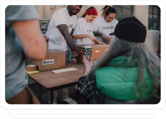 Volunteers distributing supplies to a person in need at an outdoor charity event.