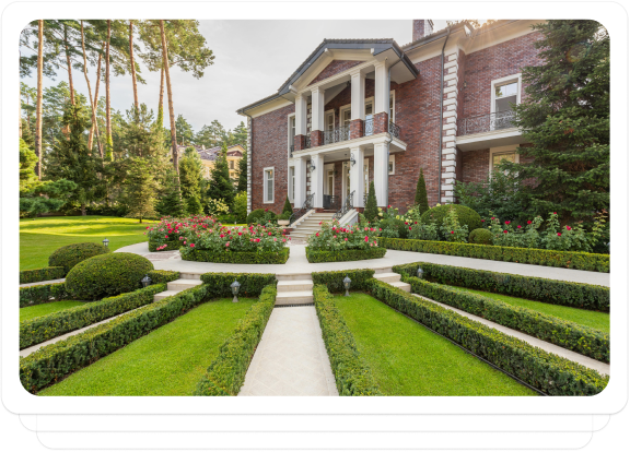 Luxury brick mansion with a landscaped garden and pathway, surrounded by trees.